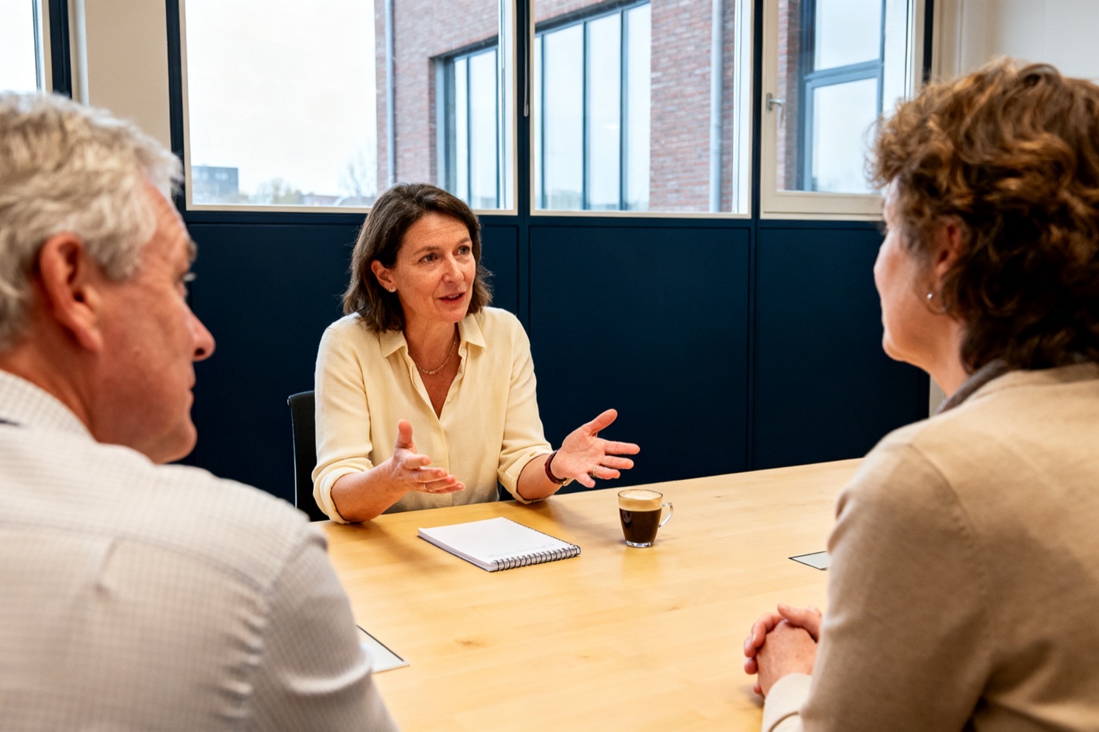 Een opdrachtgever legt aan tafel haar vraag uit aan twee ervaren mentoren, die aandachtig luisteren.